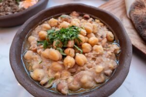 Hearty chickpea stew garnished with fresh herbs in a rustic brown bowl
