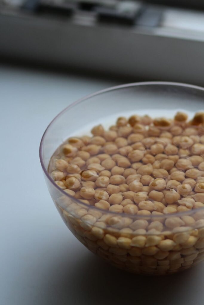 Dried chickpeas soaking in water in a clear glass bowl
