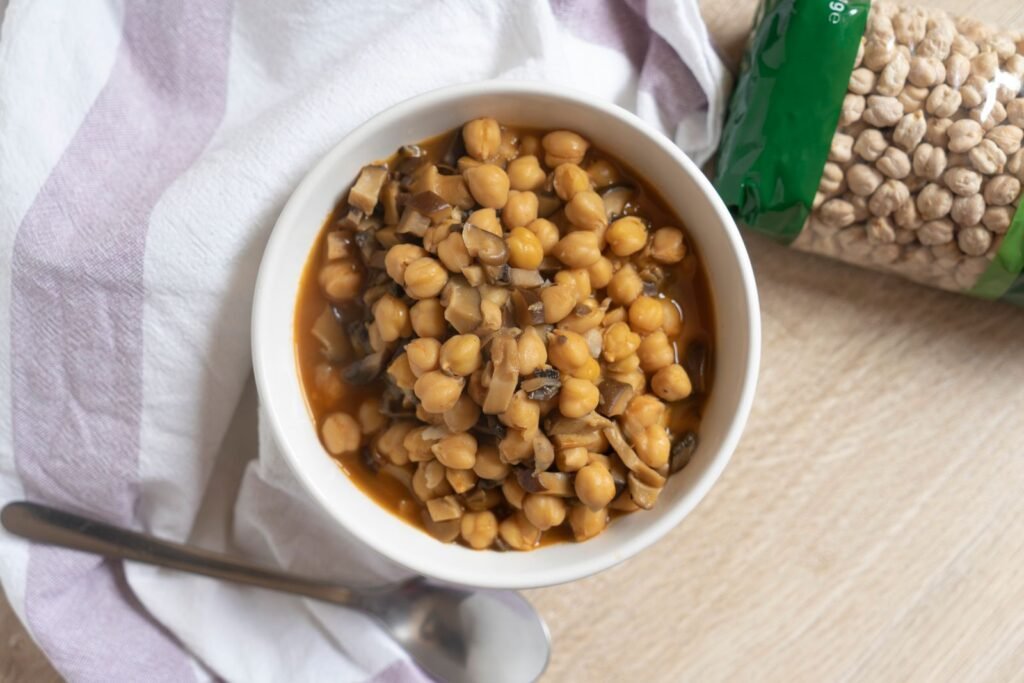 Bowl of cooked chickpeas with mushrooms next to a bag of dried chickpeas