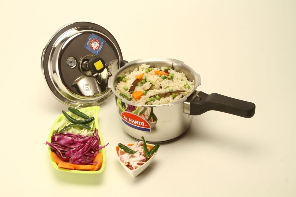 Open stainless steel stovetop pressure cooker with a cooked rice and vegetable dish